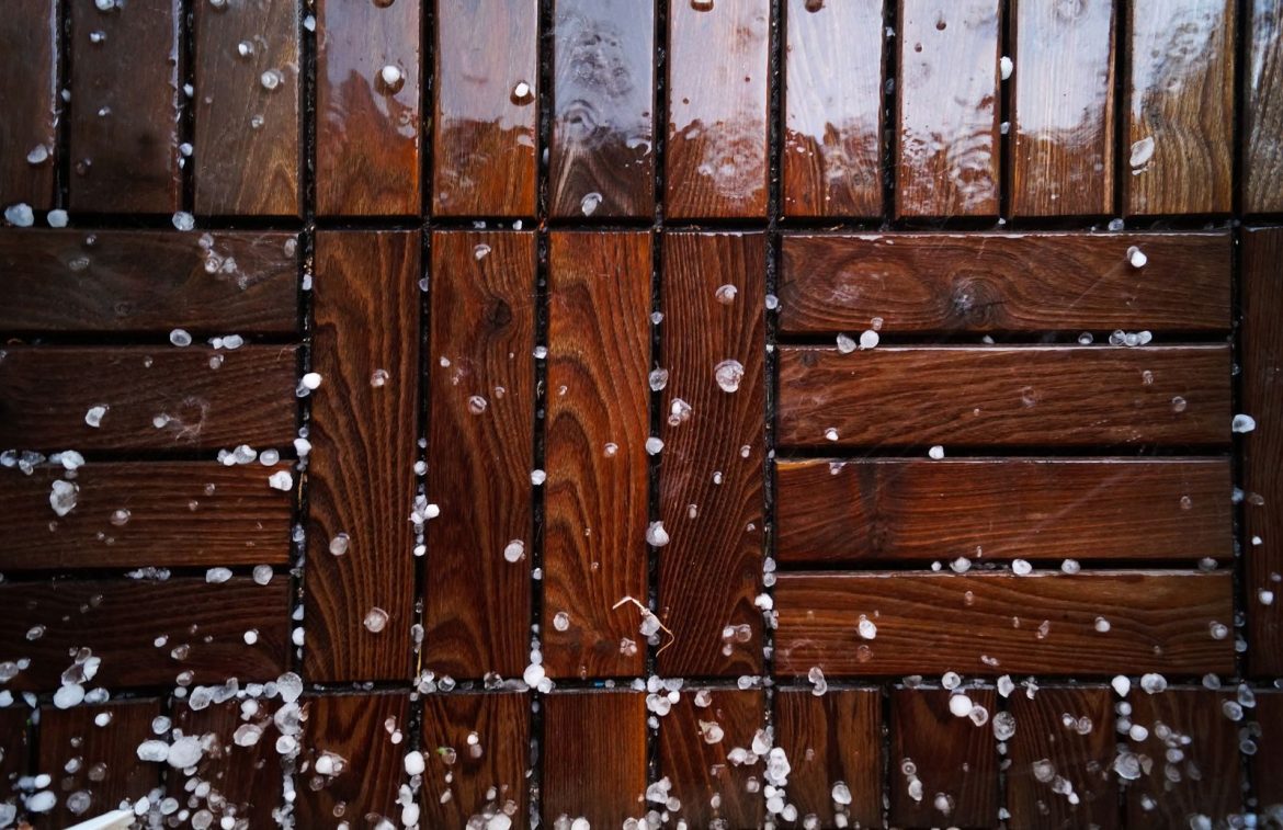 Close-up of a wet wooden deck sprinkled with sleet and snowflakes, showcasing natural texture.