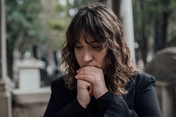 Pensive woman in black coat standing outdoors with hands together, conveying sadness.