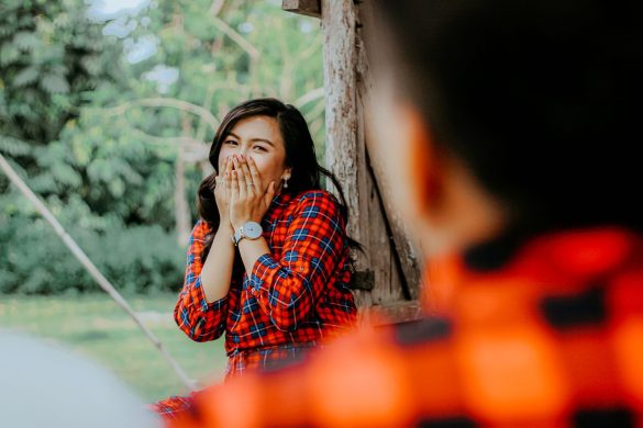 Young woman in plaid, laughing and covering mouth in a playful setting.