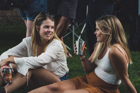 Two women sitting on grass, enjoying drinks during a casual outdoor gathering.