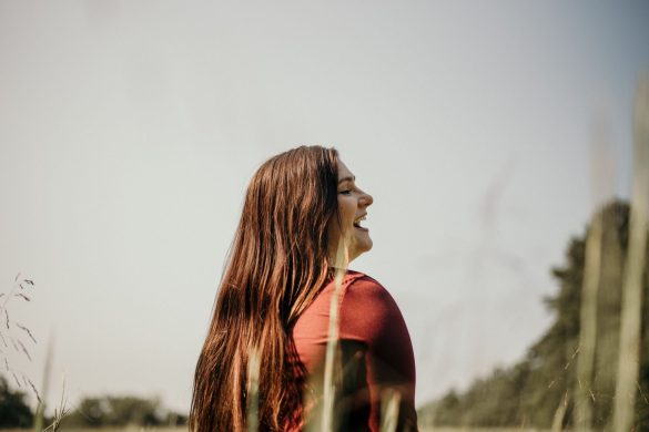 A woman with long hair smiling happily in an outdoor meadow setting.