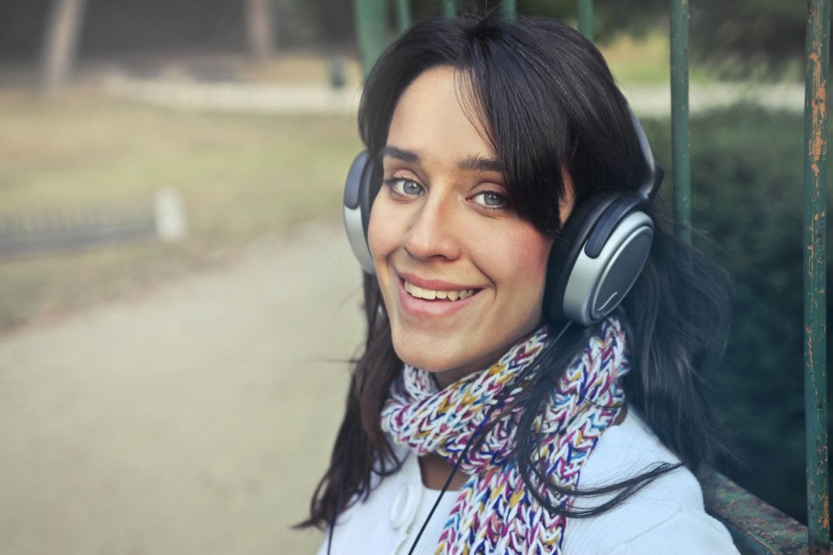 Smiling woman with headphones enjoying music outdoors on a fall day.