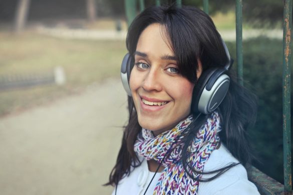 Smiling woman with headphones enjoying music outdoors on a fall day.