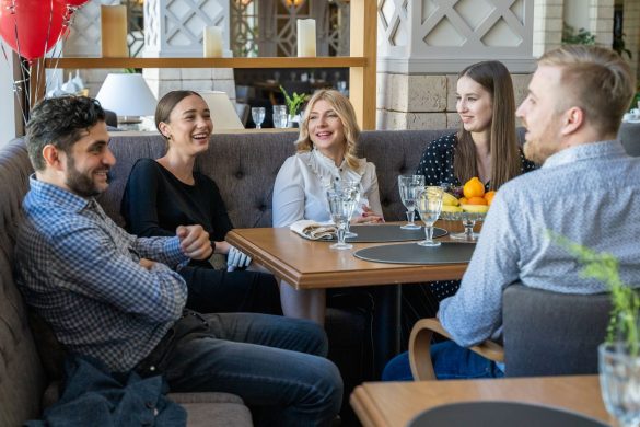 Five adults having a joyful conversation in a cozy restaurant setting indoors.