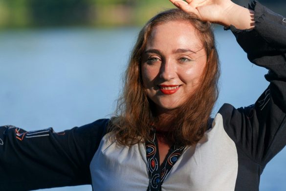 A woman with red lipstick and auburn hair posing against a blue water background